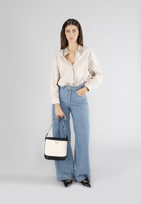 Ljusbeige knäppt skjorta med dekorativ krage, i kombination med ljusblå högmidjade vida jeans, hållande en tvåfärgad handväska. Svarta spetsiga skor.