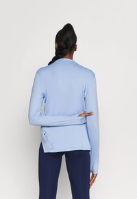 Helles blaues Langarmshirt mit glatter Textur, hoher Kragen, abgerundetem Saum und Daumenlöchern. Die Rückansicht zeigt einen figurnahen Schnitt.