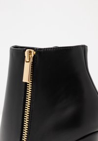 Stivale alla caviglia in pelle nera con cerniera metallica dorata di lato su sfondo bianco.