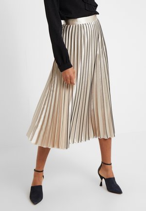 Metallic plisseret nederdel i creme med sorte lodrette striber. Har en glat linning og falder over anklen, kombineret med marineblå hæle.