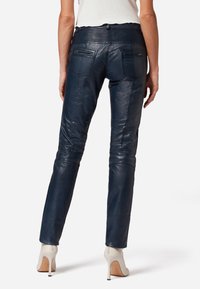 Marineblauwe leren broek met een getailleerd ontwerp, voorzien van een geribde tailleband en achterzakken; gladde textuur met een subtiele glans.