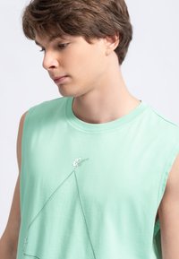 Maglietta senza maniche verde menta realizzata in morbido cotone, con un design di disegno a linee minimaliste in bianco sulla parte anteriore.