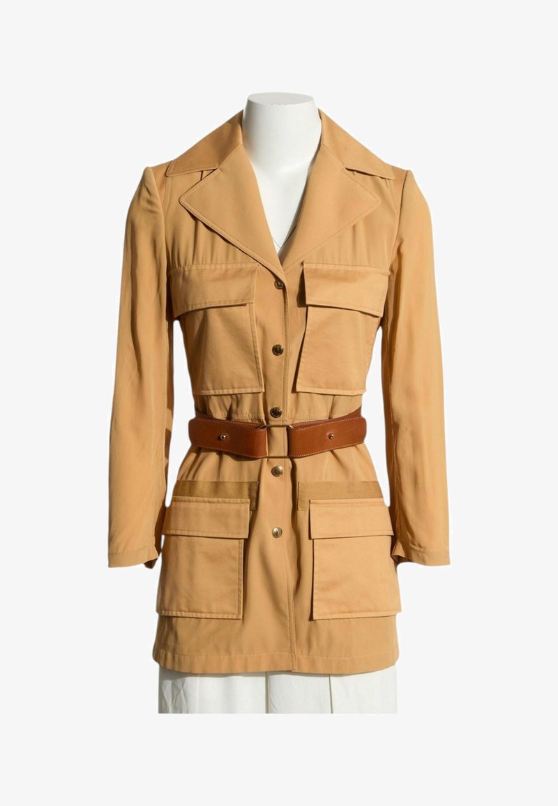 Veste longue à manches longues couleur fauve avec quatre grandes poches à rabat sur le devant, fermeture par boutons, larges revers et ceinture en cuir marron à la taille.