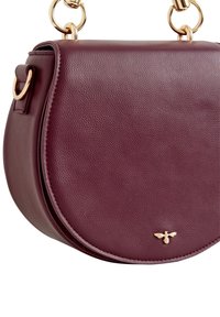 Bordowa skórzana torba na ramię o zakrzywionym kształcie, z złotymi elementami ozdobnymi i małym logo pszczoły z przodu. Widoczne szczegóły faktury powierzchni.