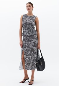 Vestido sin mangas con estampado floral en blanco y negro, con cintura peplum, abertura lateral y una silueta fluida. Combinado con un bolso negro.