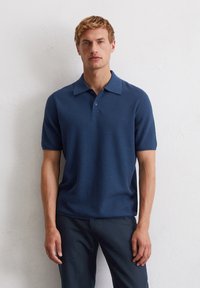 Marineblauwe polo met een textuurgebreide stof, korte mouwen en een platte kraag, voorzien van een drieknoopsluiting en subtiele ontwerpdetails.