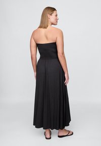 Czarna sukienka maxi bez ramiączek, wykonana z gładkiej, elastycznej tkaniny. Charakteryzuje się dopasowanym gorsetem i zwiewną spódnicą z subtelnymi zakładkami zaczynającymi się od talii.
