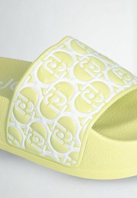 Sandale slide jaune et blanche avec semelle texturée et bride arborant un motif circulaire en relief répété.