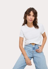 Maglietta bianca in cotone con scollo rotondo, maniche corte e vestibilità comoda, abbinata a jeans azzurri a vita alta e cintura marrone chiaro.