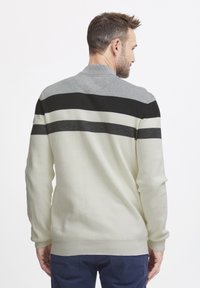 Light-colored sweater featuring a ribbed texture, with black and gray horizontal stripes across the back and a small collar detail.