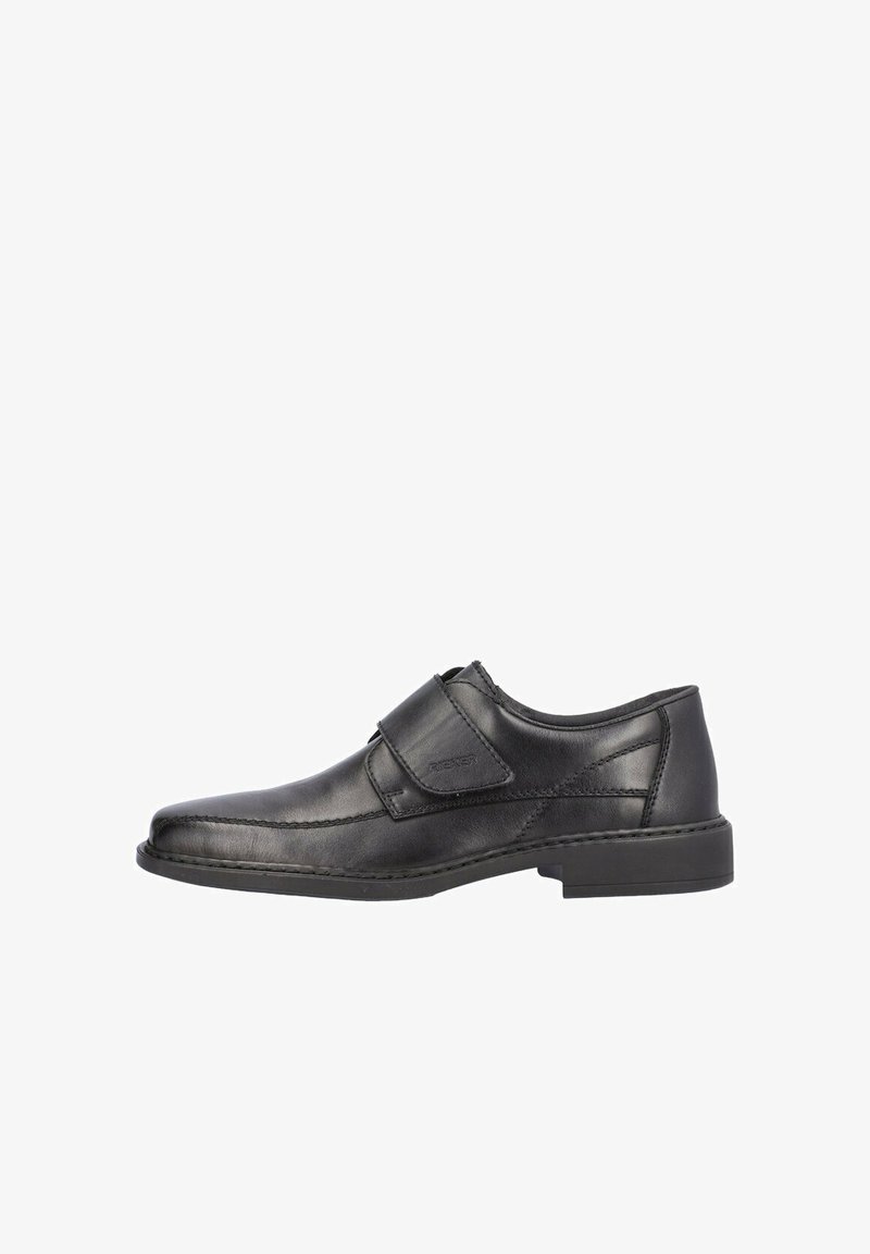 Chaussure en cuir noire avec une semelle plate, un bout rond et une sangle Velcro réglable. Présente des détails de surpiqûres croisées et une texture lisse.