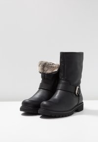 Bottes en cuir noir avec une finition texturée, bord en fausse fourrure, sangle réglable avec des pièces métalliques, et semelle robuste pour une bonne traction.