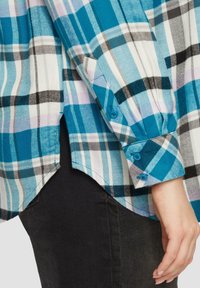 Camicia a quadri nei toni di blu, bianco e nero, con polsini con bottone e orlo curvo. Realizzata in tessuto tessuto con una texture liscia.