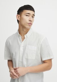 Camisa blanca de manga corta con botones, hecha de un tejido ligero, que cuenta con un bolsillo en el pecho y un cuello clásico. Textura suave.