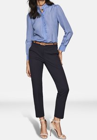 Light blue blouse with ruffled front, long sleeves, and buttoned collar, paired with dark navy tailored pants and beige high-heel sandals.