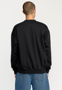 Black sweatshirt with a round neck, dropped shoulders, and ribbed cuffs. Smooth fabric texture. Worn with light blue tapered jeans.