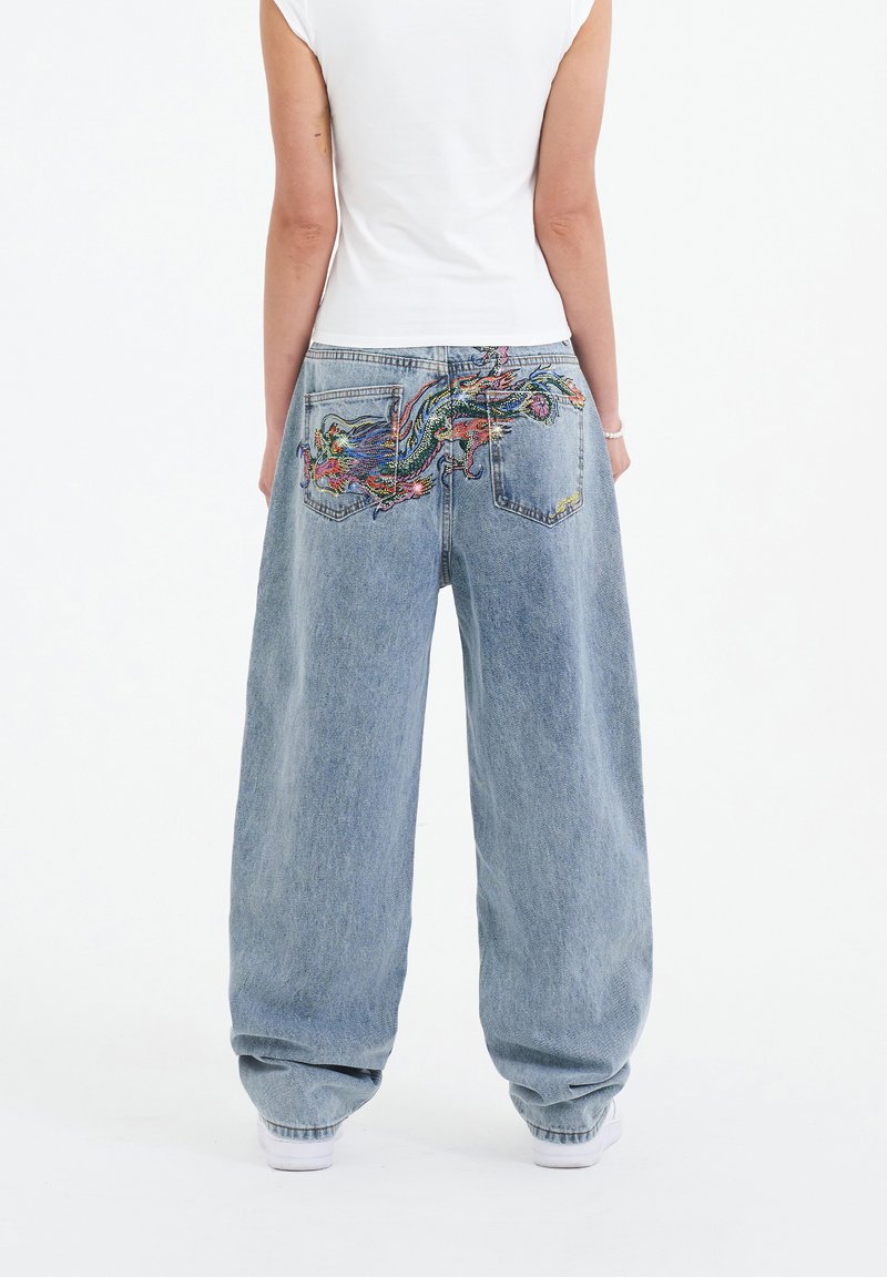 Light wash, wide-leg denim jeans feature colorful embroidered design on the back pockets. Fabric shows a soft, textured finish.