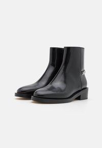 Black leather ankle boots with a sleek design, featuring a round toe, low stacked heel, and a decorative chain accent on the side.