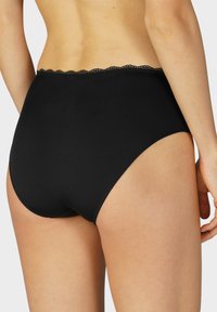Mutande nere a vita alta con una texture liscia e un bordo in pizzo ondulato lungo l'elastico in vita, dotate di una vestibilità sagomata sul retro.