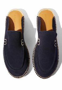 Granatowe zamszowe mokasyny na plecionym jucie, z dwiema srebrnymi klamrami i kontrastowym przeszyciem wzdłuż brzegów. Gładka tekstura.