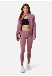 Athletic outfit featuring a long-sleeved, light purple zip-up jacket, black sports bra, and matching high-waisted leggings. White sneakers.