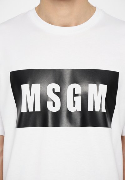 White cotton t-shirt with a black rectangular graphic featuring bold white letters "MSGM" in the center. Soft texture, crew neckline.