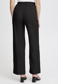Pantalons noirs à larges jambes en tissu léger avec une finition texturée. Présente une taille élastique et tombe jusqu'à la cheville.
