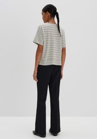 Black and white patterned short-sleeve top with a straight cut, paired with high-waisted black trousers. Simple flat shoes complete the look.