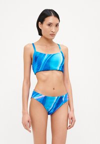 Bikini set so žíhaným modrým vzorom pozostávajúci z topu so štvorcovým výstrihom a zodpovedajúcich nízko strihaných nohavičiek, vyrobený z hladkého, elastického materiálu s lesklým povrchom.