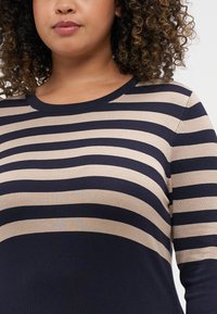 Pull à manches longues en tricot avec des rayures horizontales bleu marine et beige. Encolure ronde, texture moyenne et coupe ajustée, mettant en valeur la silhouette.