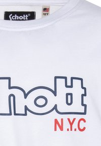Camiseta de algodón blanca con un llamativo logo de "Schott" en azul marino y texto en rojo "N.Y.C.". Incluye un cuello redondo y etiqueta con la talla 12Y.