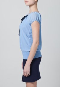 Top corto de manga corta azul claro con hombros fruncidos y detalle de lazo en navy. Diseño ceñido y dobladillo acanalado combinado con una falda navy.
