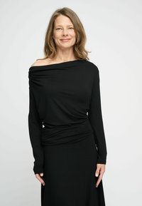 Crna bluza s dugim rukavima i off-shoulder dizajnom, s drapiranim teksturama i naboranim detaljem u struku, uparen s odgovarajućom suknjom.