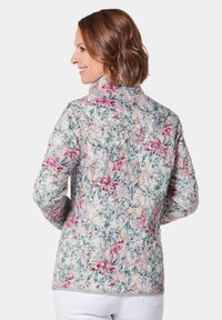 Quilted Jacke mit floralem Muster in Rosa, Grün und Blau, mit Stehkragen und langen Ärmeln, von hinten gezeigt.