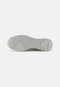 Semelle d'une chaussure gris clair avec des motifs géométriques en relief et le nom de la marque "Michael Kors" imprimé près du talon.