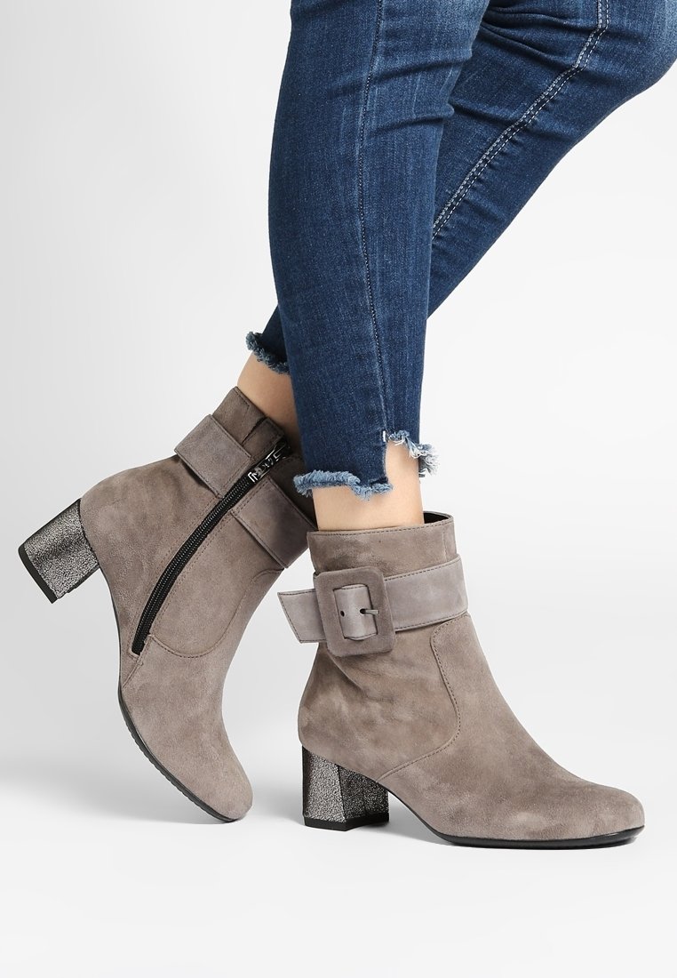 Botines de ante gris con tacón grueso, cremallera lateral y una correa decorativa con hebilla, con un detalle plateado texturizado en el tacón.