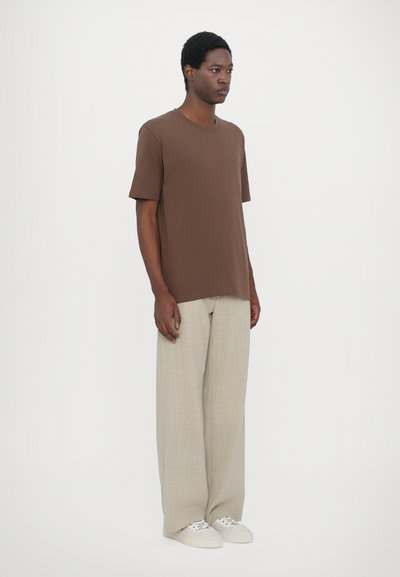 Brown short-sleeve T-shirt with a round neck, pocket detail; paired with light beige wide-leg trousers and white sneakers.