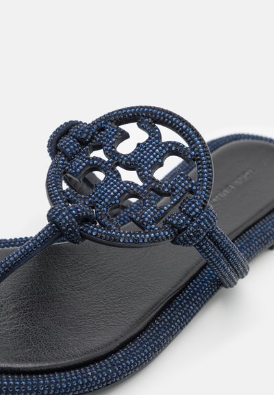 Navy blue thong sandals with textured straps and a circular cutout accent adorned with small blue studs on the top. Black cushioned footbed.
