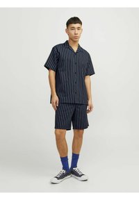 Trumpu rankoviu dryžuotu marškinėliu ir atitinkamais šortais tamsiai mėlynos spalvos su baltais vertikaliais dryžiais. Dėvimi su mėlynos spalvos kojinėmis ir juodais sportbačiais.