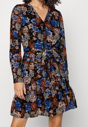 Woman wearing a long-sleeve, V-neck floral dress with a tie waist, featuring blue, brown, and gray flowers on a black background.