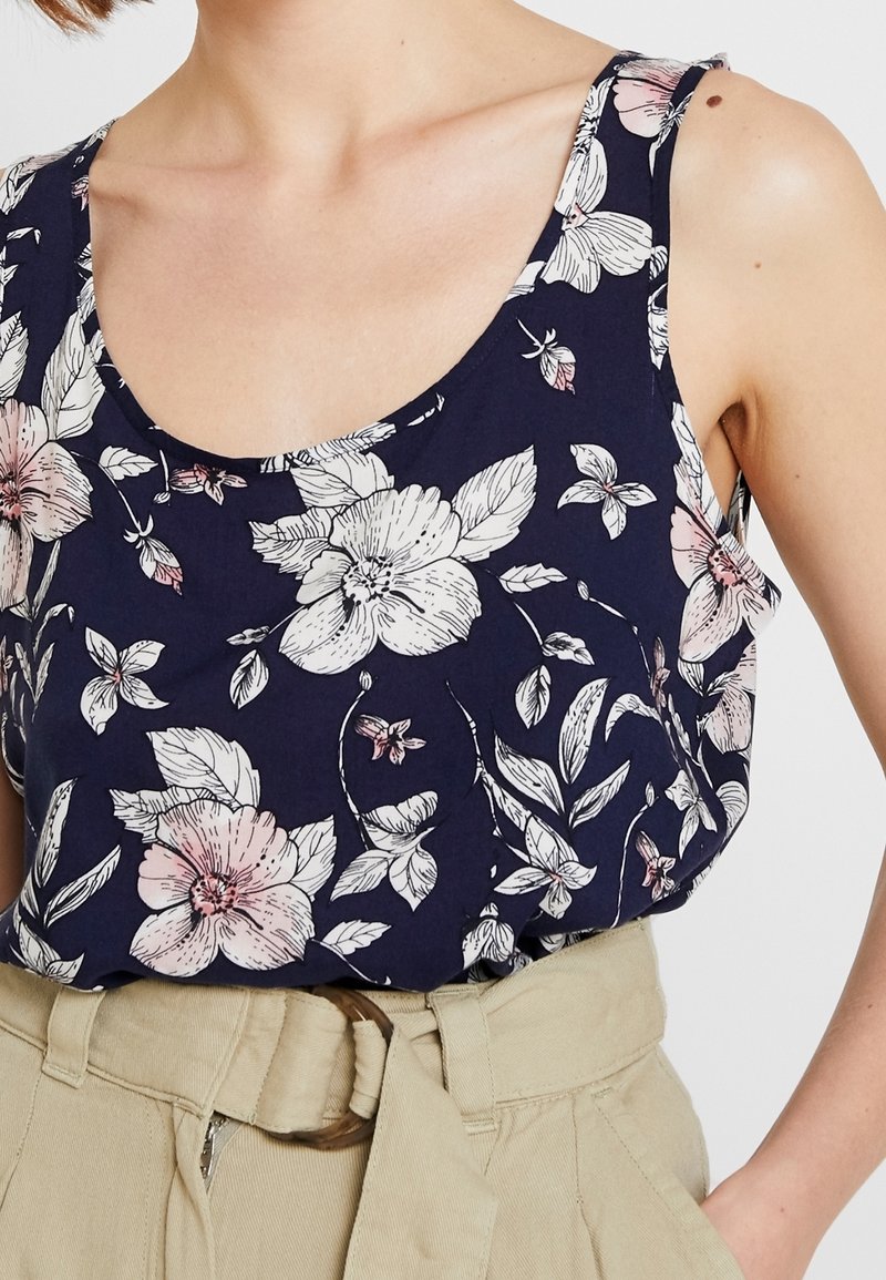 Ärmeloses Blumenshirt aus marineblauem Stoff, mit großen rosa und weißen Blumen sowie grünen Blättern, Rundhalsausschnitt und weicher Textur.