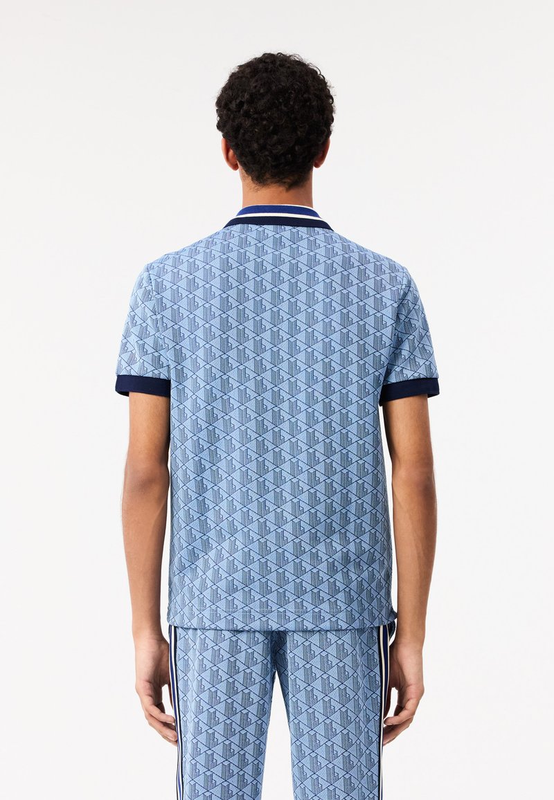 Chemise polo bleu à motifs avec un design en losange, col marine et manches courtes. Le matériau semble doux, avec un pantalon bleu assorti en dessous.
