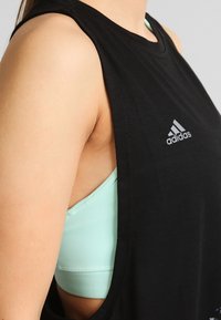 Czarny bezrękawnik z miękkiego materiału z dużymi otworami na ramionach, z srebrnym logo Adidas na piersi, w połączeniu z miętową sportową bielizną pod spodem.