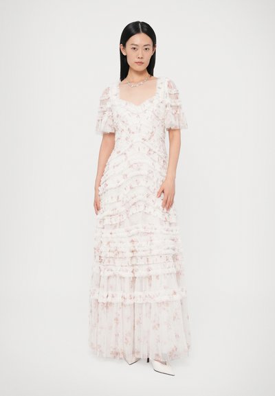 Biele šaty s kvetinovou potlačou, volánovou textúrou, balónovými rukávmi a jemne zvýrazneným výstrihom, ktoré splývajú až na zem. Nosia sa s bielymi lodičkami.