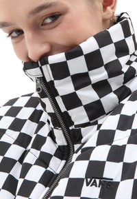 Giacca puffer a scacchi bianco e nero con colletto alto, zip intera e logo ricamato "VANS". Materiale liscio e lucido.