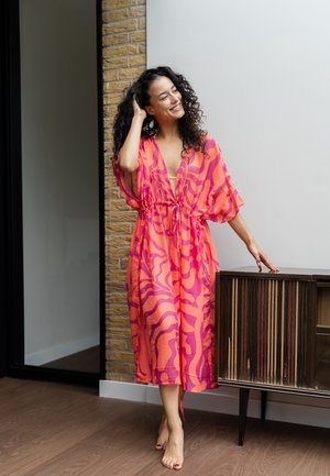 Roze en oranje gemarmerde kaftan met een strik taille, doorschijnende stof, korte mouwen en een diepe V-halslijn, gecombineerd met een houten kast.