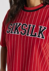 Punainen raidoitettu T-paita, joka on valmistettu pehmeästä puuvillasta. Edessä musta brodeerattu teksti "SIKSILK" ja kontrastina musta kaula-aukko.
