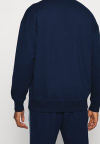 Felpa blu navy con vestibilità rilassata, polsini e orlo a coste, e una texture morbida. Presenta una finitura liscia e dettagli minimi sul retro.