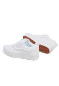 White canvas sneakers with a low profile, round toe, flat laces, and a textured brown rubber sole. Features a side stripe design.
