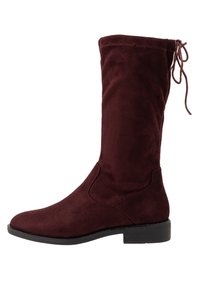 Bottes hauteur genou en suède bourgogne avec un bout arrondi, des détails de couture intérieure et un accent de nœud en haut. Talon bas empilé noir.